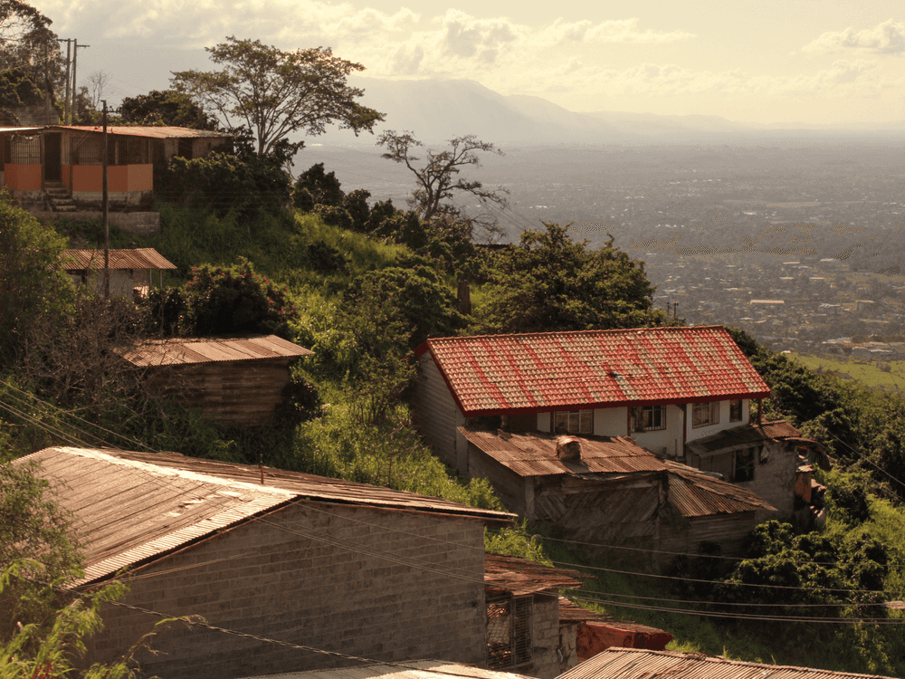 Casas de techo rojo en la ladera de Aserrí, con el Valle Central y sus montañas al fondo en la tarde