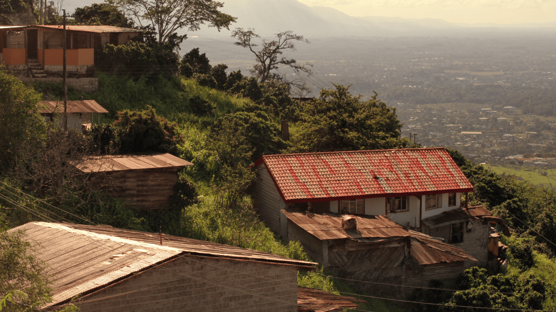 Casas de techo rojo en la ladera de Aserrí, con el Valle Central y sus montañas al fondo en la tarde