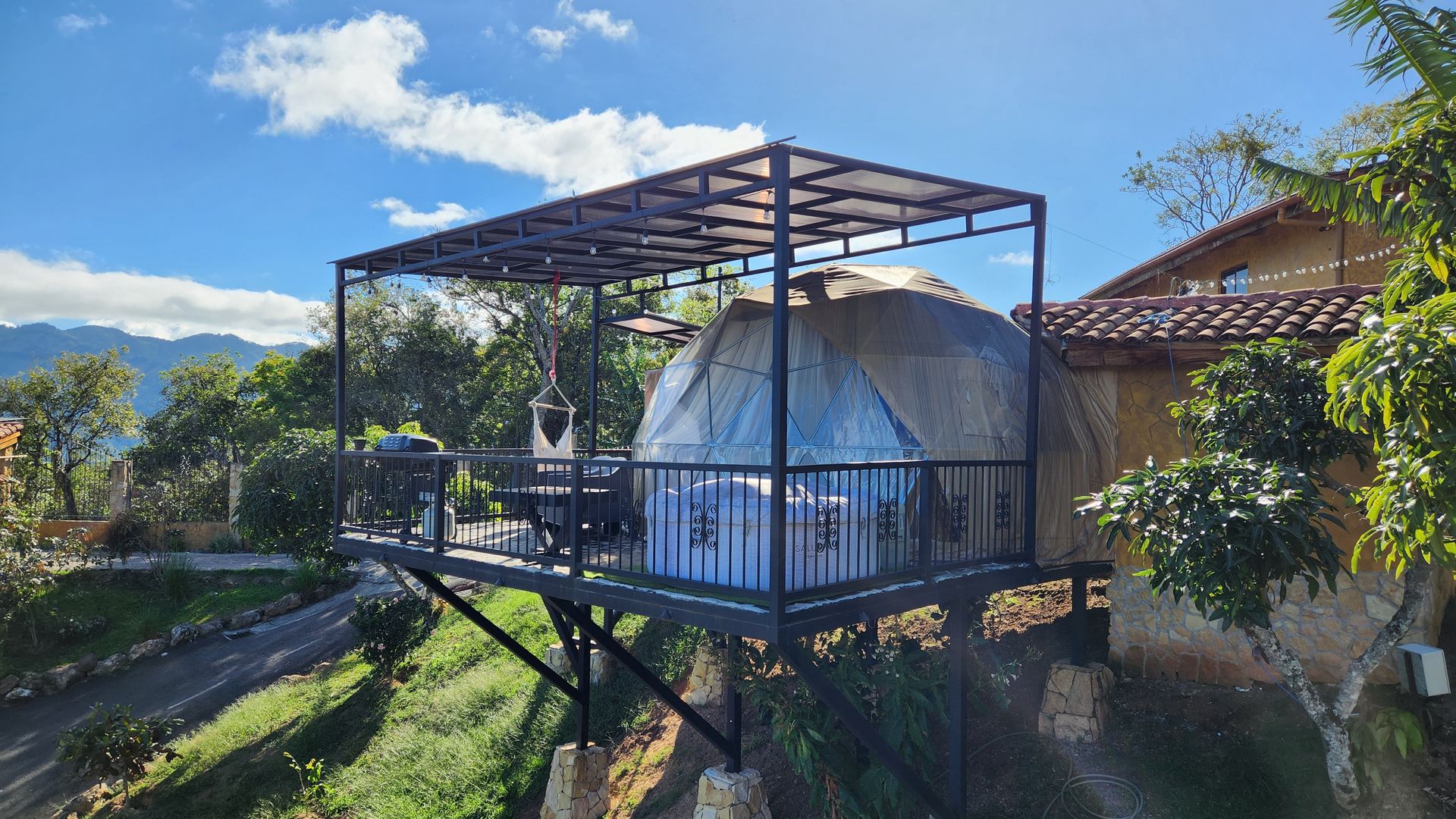 El domo geodésico sobre una plataforma elevada con techo propio, jacuzzi en la terraza y las montañas del valle de fondo
