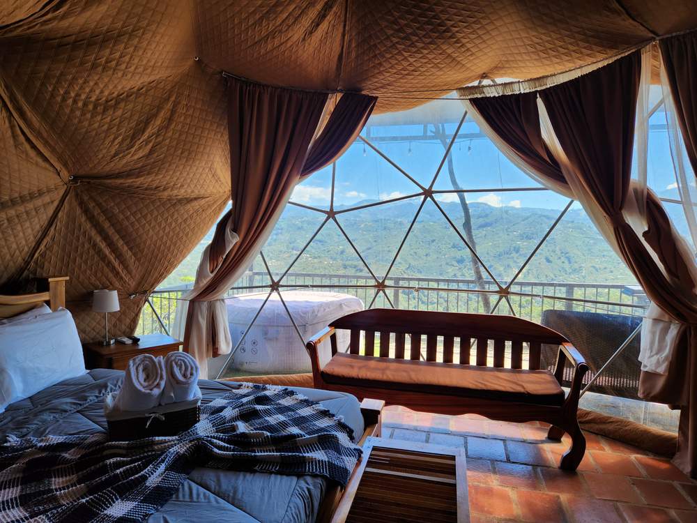 Interior del domo con cama doble, banca de madera y ventana geodésica con vista a las montañas