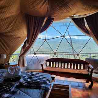 Interior del domo con cama doble, banca de madera y ventana geodésica con vista a las montañas