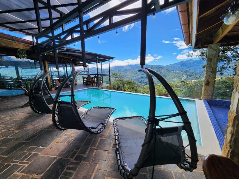 Terraza junto a la piscina infinita con camastros colgantes y vista a las montañas de Aserrí