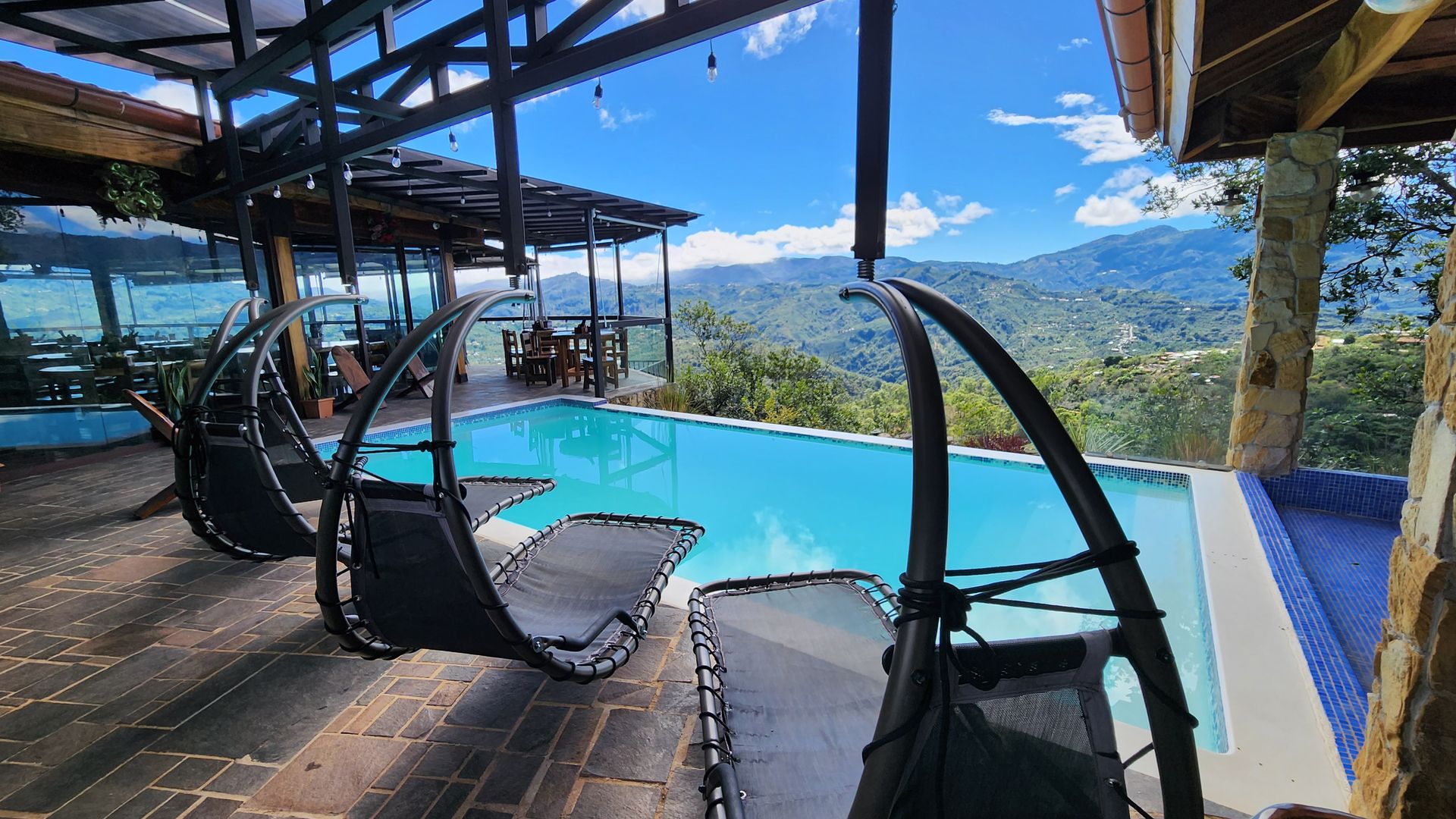 Terraza junto a la piscina infinita con camastros colgantes y vista a las montañas de Aserrí