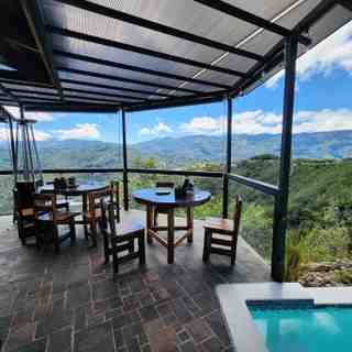 Mesas redondas de madera en la terraza techada, junto al borde de la piscina y con vista a las montañas