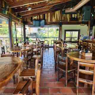 Comedor interior con mesas y sillas de madera rústica, piso de ladrillo y la barra al fondo