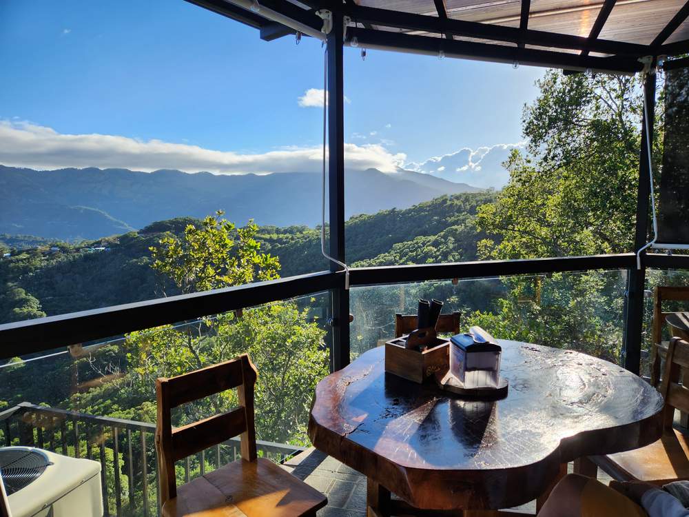Mesa de madera junto al ventanal, con servilletero y vista a las montañas al atardecer
