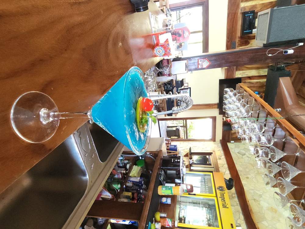 Coctel azul con cereza y limón servido en copa, sobre la barra de madera
