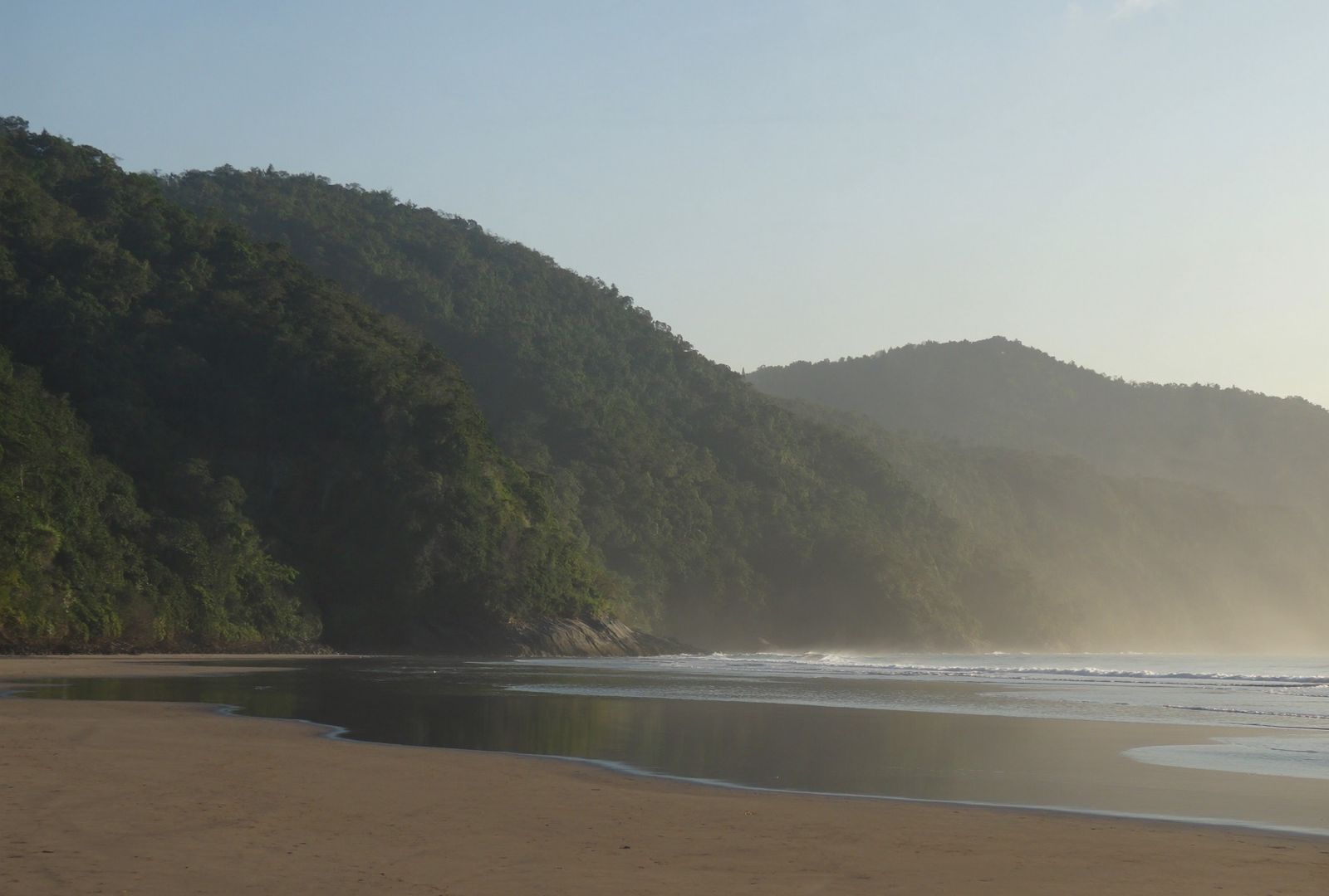 Cordilleras boscosas que bajan hasta el mar en capas de neblina, con la playa ancha descubierta por la marea baja